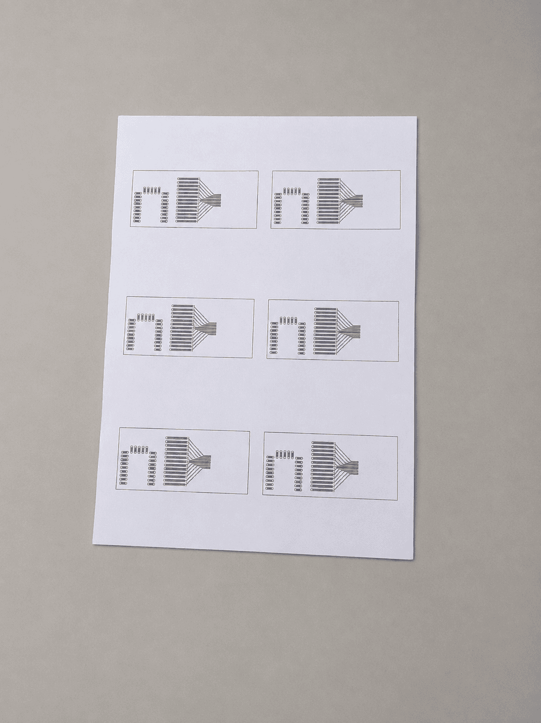 A sheet of photo paper printed with six copies of the same small PCB layout in black toner
